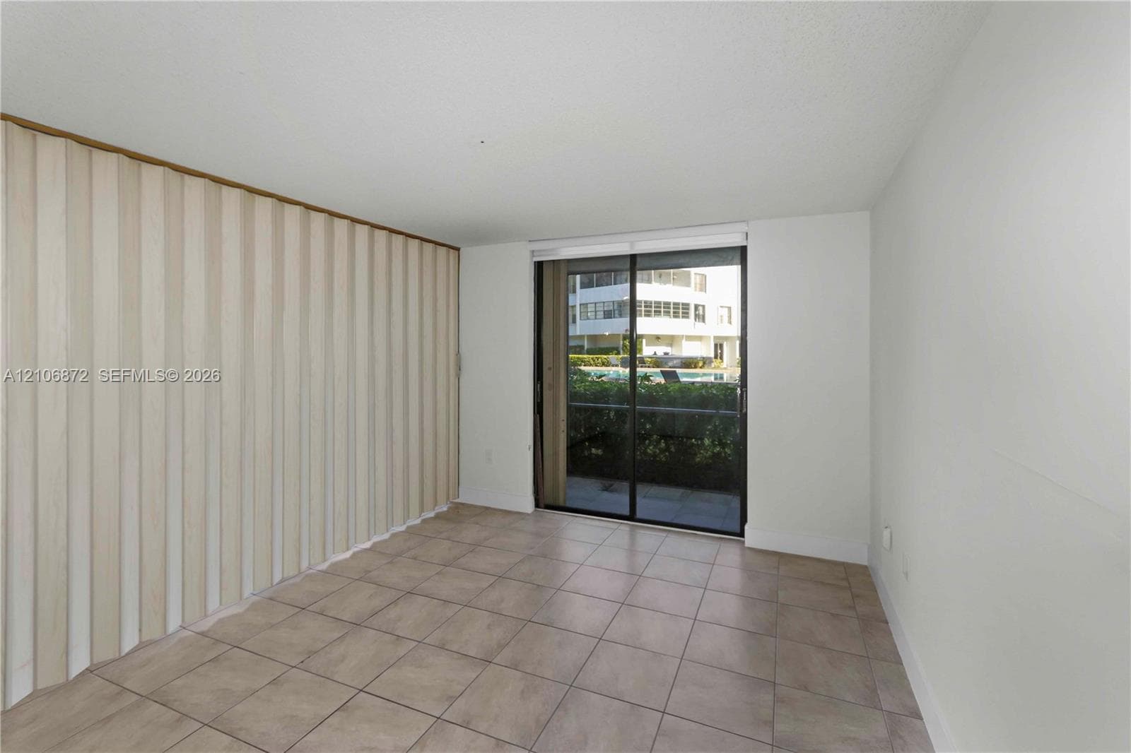 Room with neutral ceramic tile flooring, floor-to-ceiling accordion partition wall, and sliding glass door