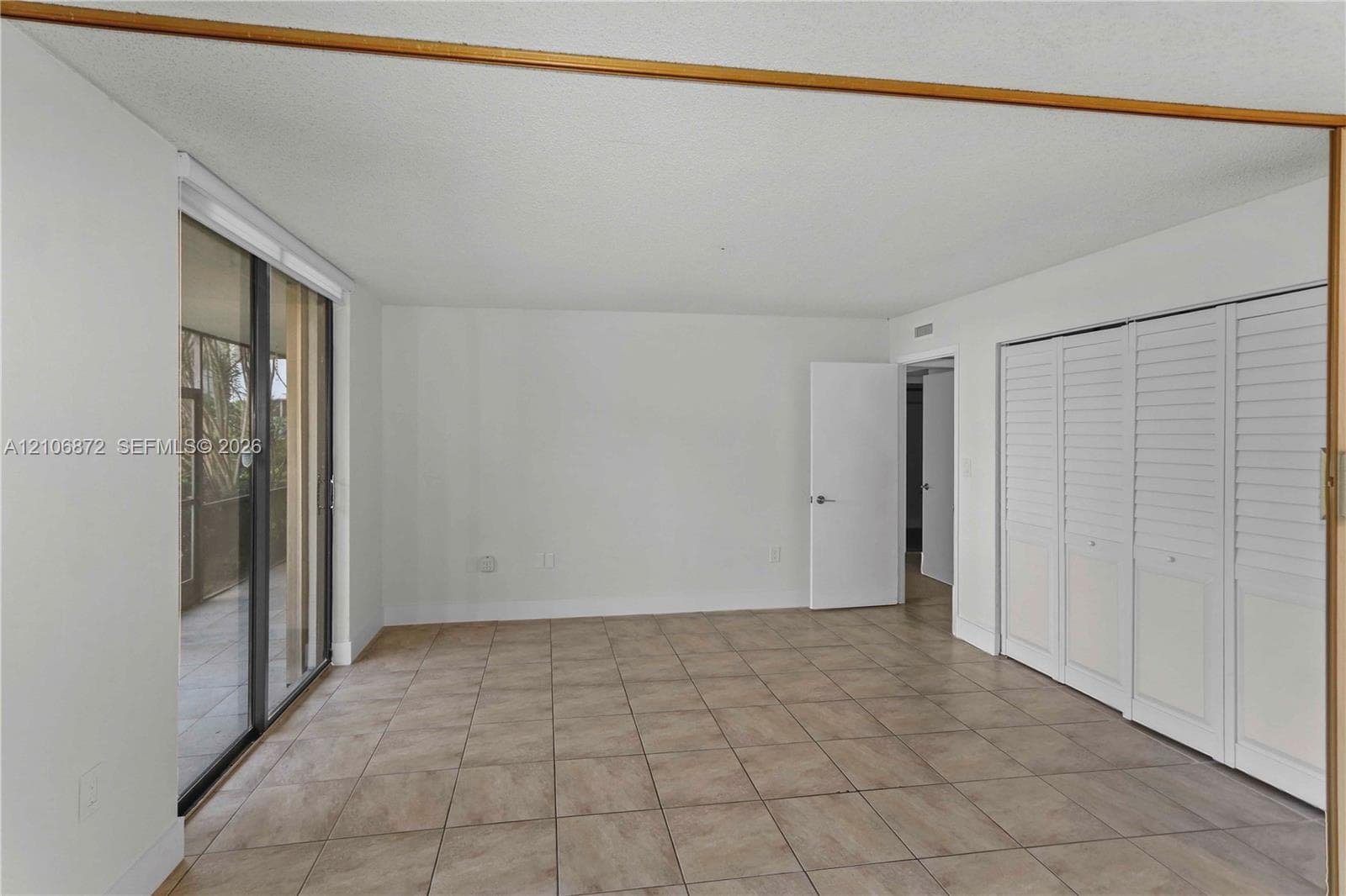 Neutral interior space featuring tile flooring, floor-to-ceiling glass sliding doors, and white louvered closet doors