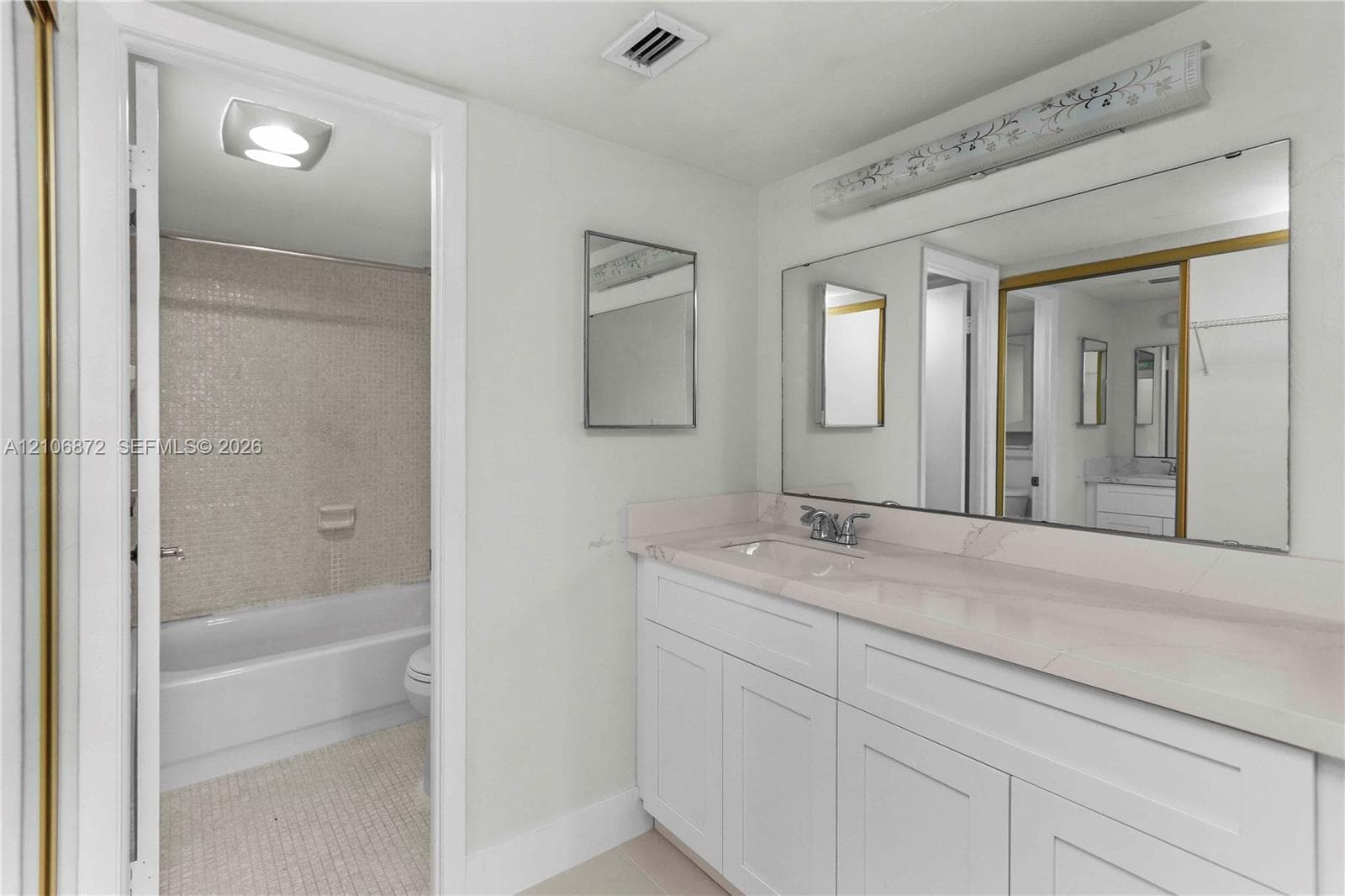 Bathroom featuring a vanity with white cabinetry and a stone-finish countertop, a large wall-mounted mirror, and a tile-surround bathtub
