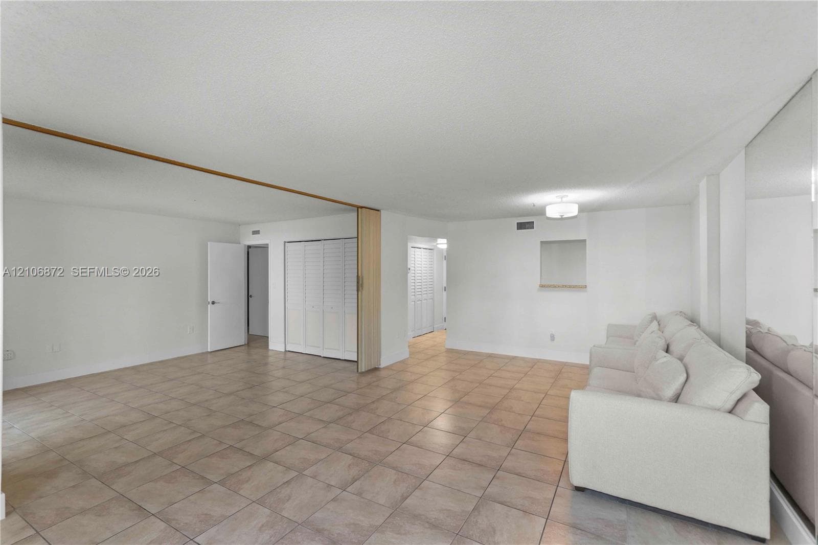 Open-concept floor plan with ceramic tile flooring, mirrored wall paneling, built-in louvered closet doors, and a decorative interior pass-through window