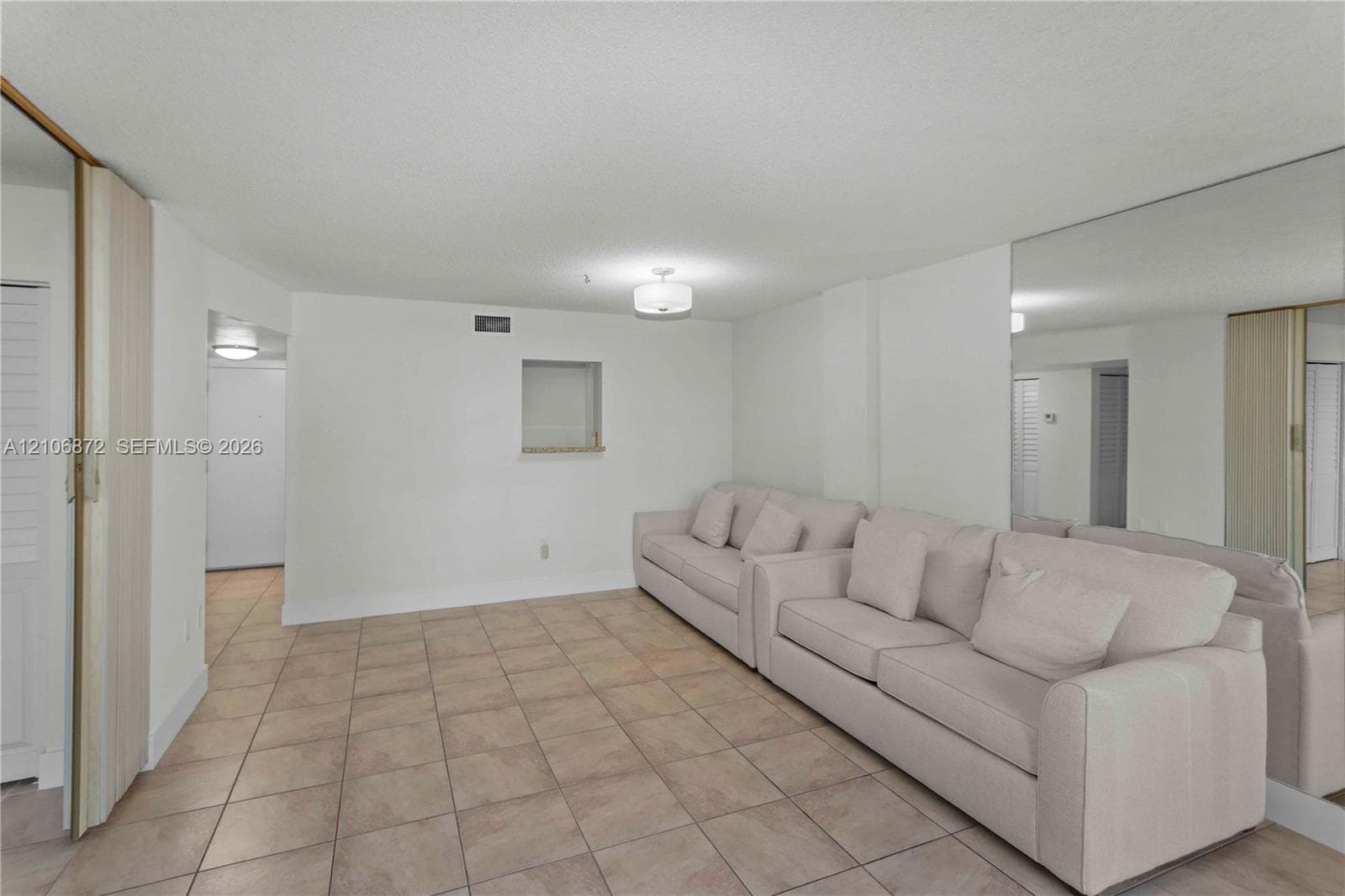 Neutral-toned tile flooring, floor-to-ceiling wall-mounted mirror, inset wall niche, and flush-mount lighting fixtures