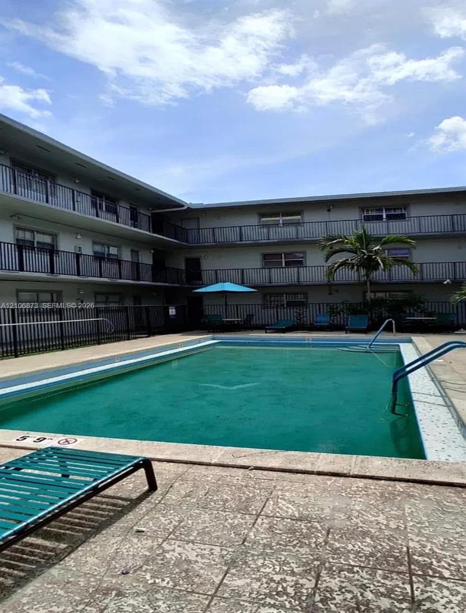 Swimming pool with concrete decking, metal perimeter fencing, and multi-story exterior balconies