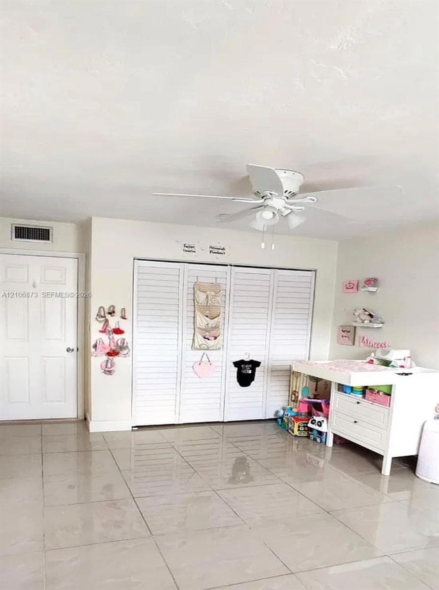 Neutral tile flooring, white bi-fold closet doors, and a ceiling fan with integrated lighting