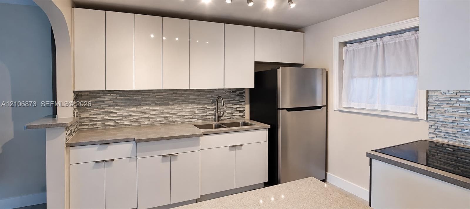 Kitchen featuring flat-panel cabinetry, multi-tonal linear tile backsplash, solid surface countertops, stainless steel appliances, and track lighting