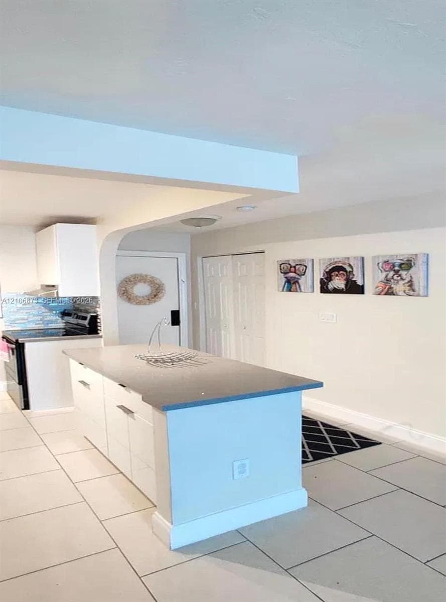Kitchen featuring a central island with a solid surface countertop, white cabinetry, tile flooring, and a blue tile backsplash