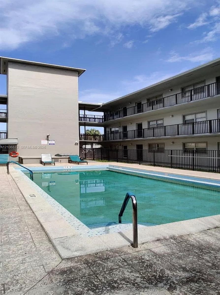 In-ground swimming pool with a concrete deck, metal pool railing, and perimeter security fencing