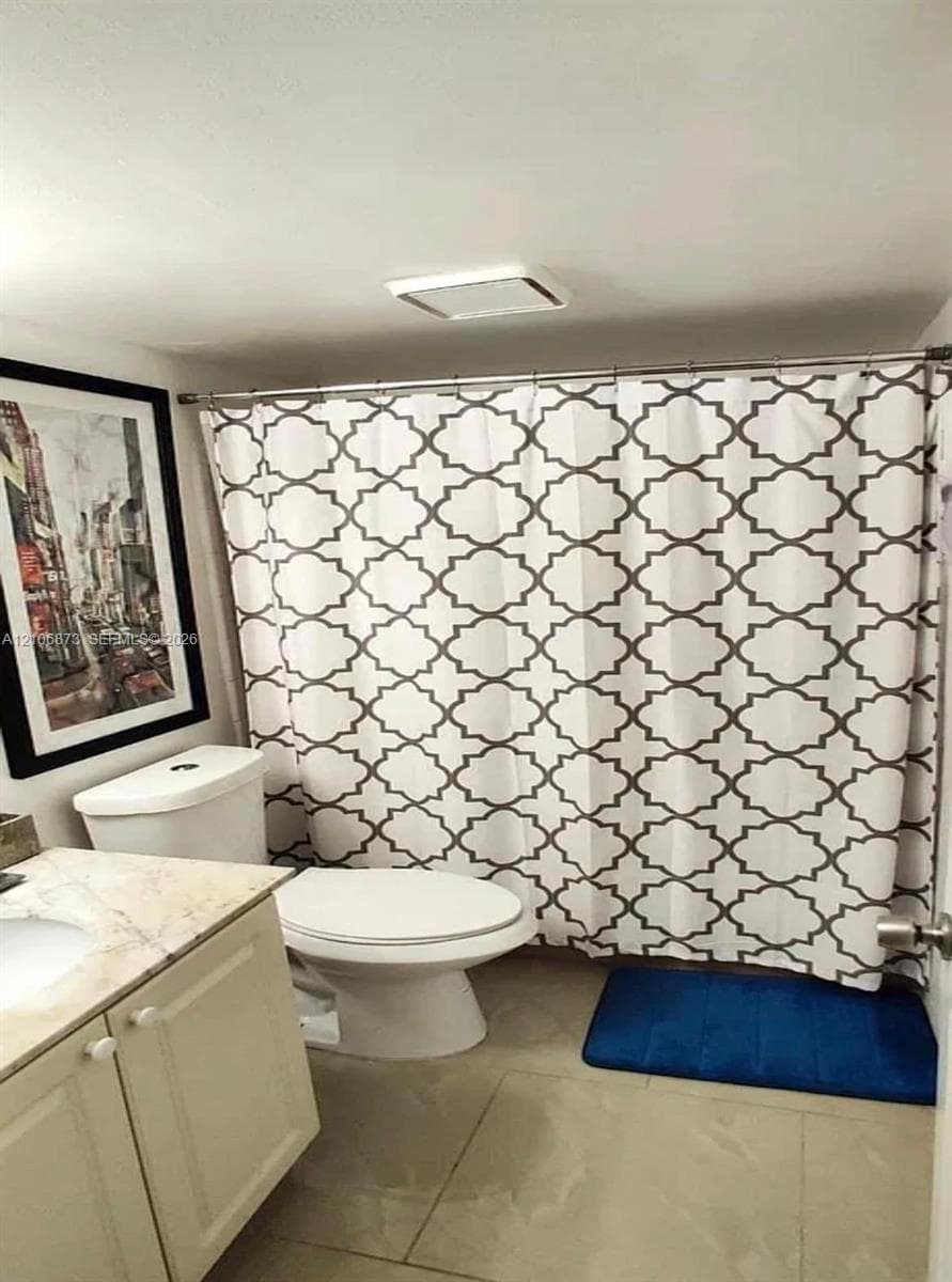 Bathroom featuring a light-toned vanity with a stone-finish countertop, an integrated sink, a neutral-toned toilet, and large-format floor tiling
