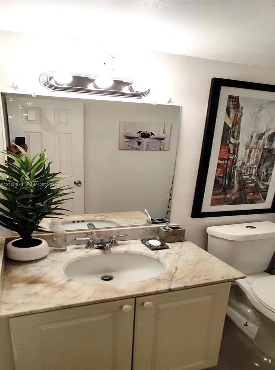 Vanity featuring a light-toned stone-finish countertop, integrated oval basin, polished chrome hardware, and white shaker-style cabinetry with a wall-mounted light fixture above the vanity mirror