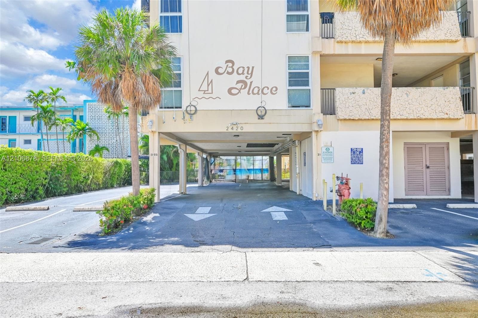 Exterior elevation featuring covered parking, concrete structure, mature palm trees, and balcony railings