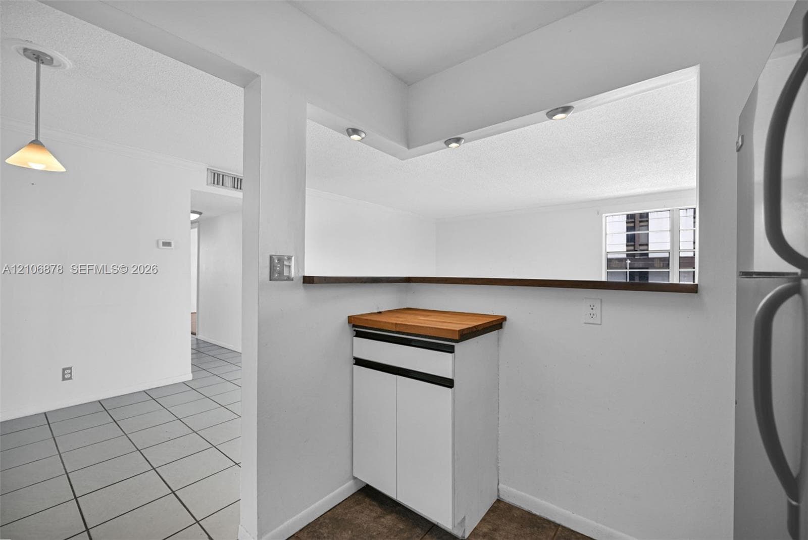 Kitchen pass-through window with wood countertop, neutral tile flooring, recessed ceiling lighting, and single-pendant light fixture