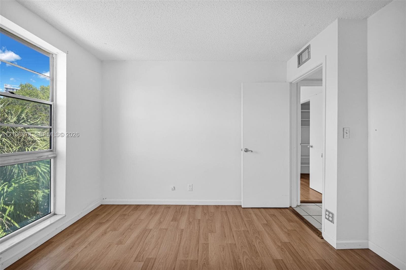 Neutral room featuring wood-finish flooring, a large single-pane window, and a built-in closet