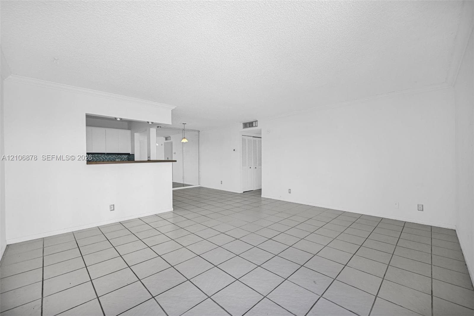 Open living area featuring neutral tile flooring, a pass-through opening, and white cabinetry