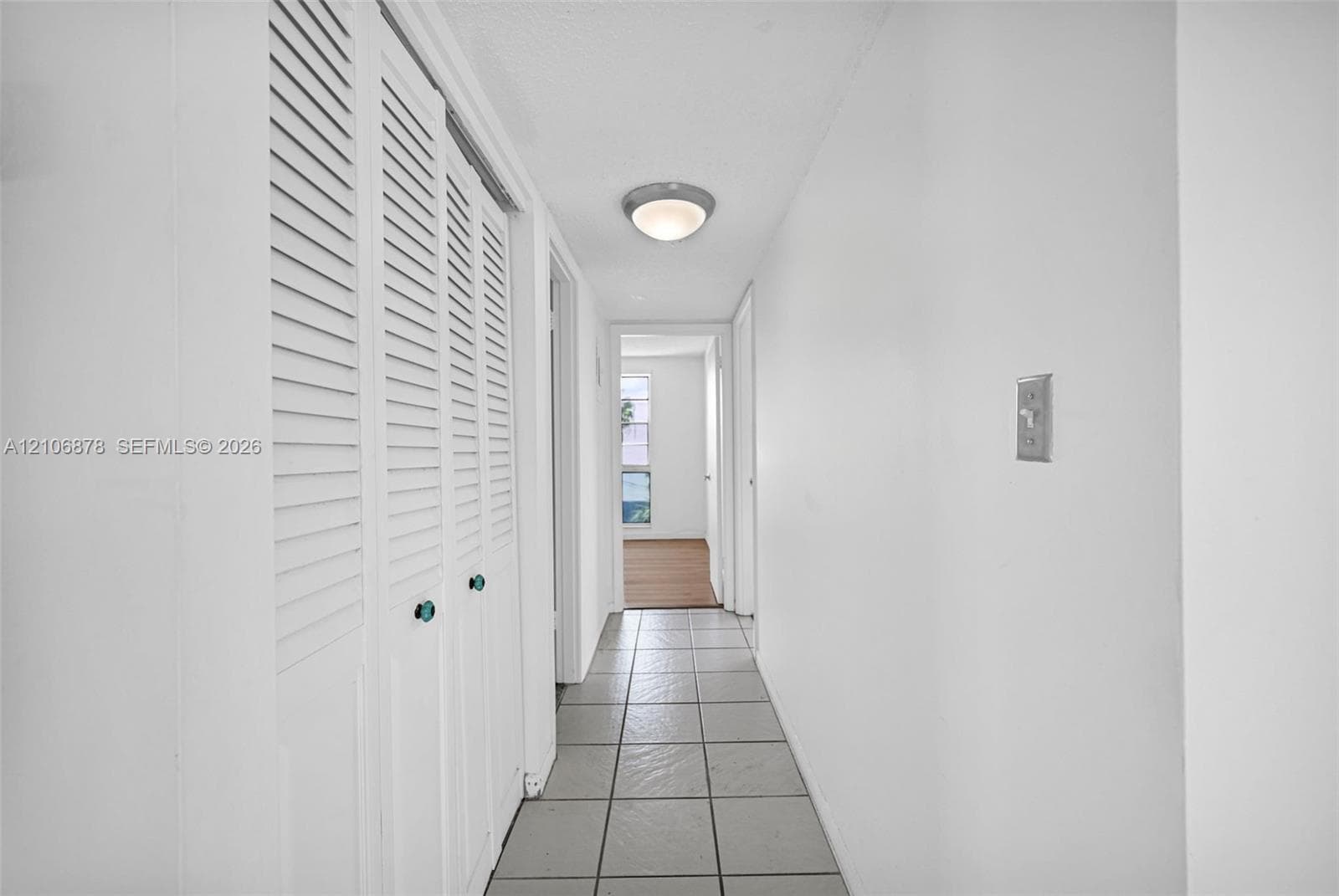 Hallway featuring tile flooring, white louvered closet doors, and a flush-mount ceiling light fixture