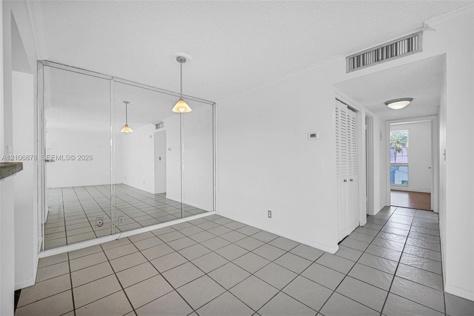 Neutral-toned ceramic tile flooring, floor-to-ceiling mirrored wall paneling, pendant light fixture, and louvered closet doors