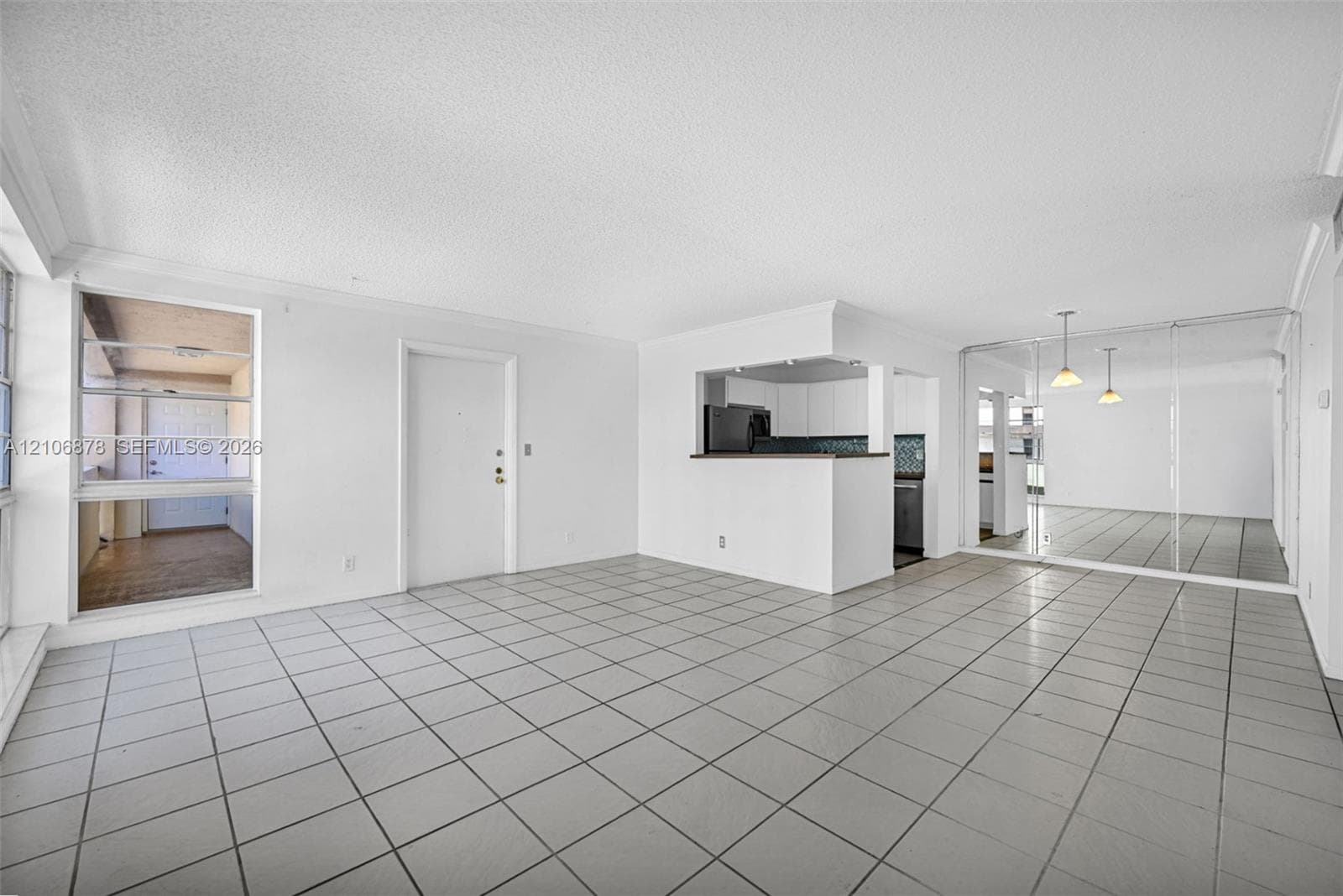 Open floor plan featuring neutral ceramic tile flooring, built-in kitchen pass-through counter, mirrored wall paneling, and dual-pane window installation