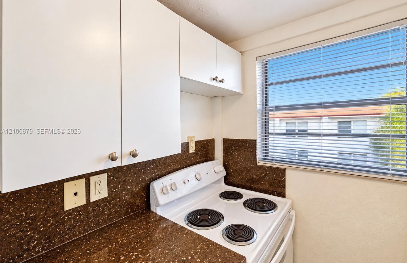 Kitchen featuring white cabinetry, dark stone-finish countertops, coordinating backsplash, and a four-burner electric range