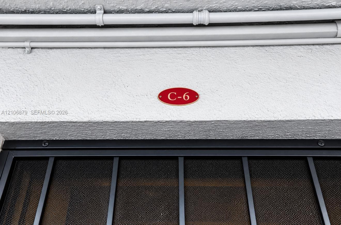 Textured stucco exterior wall featuring a red oval unit identification plaque and a black metal screen door