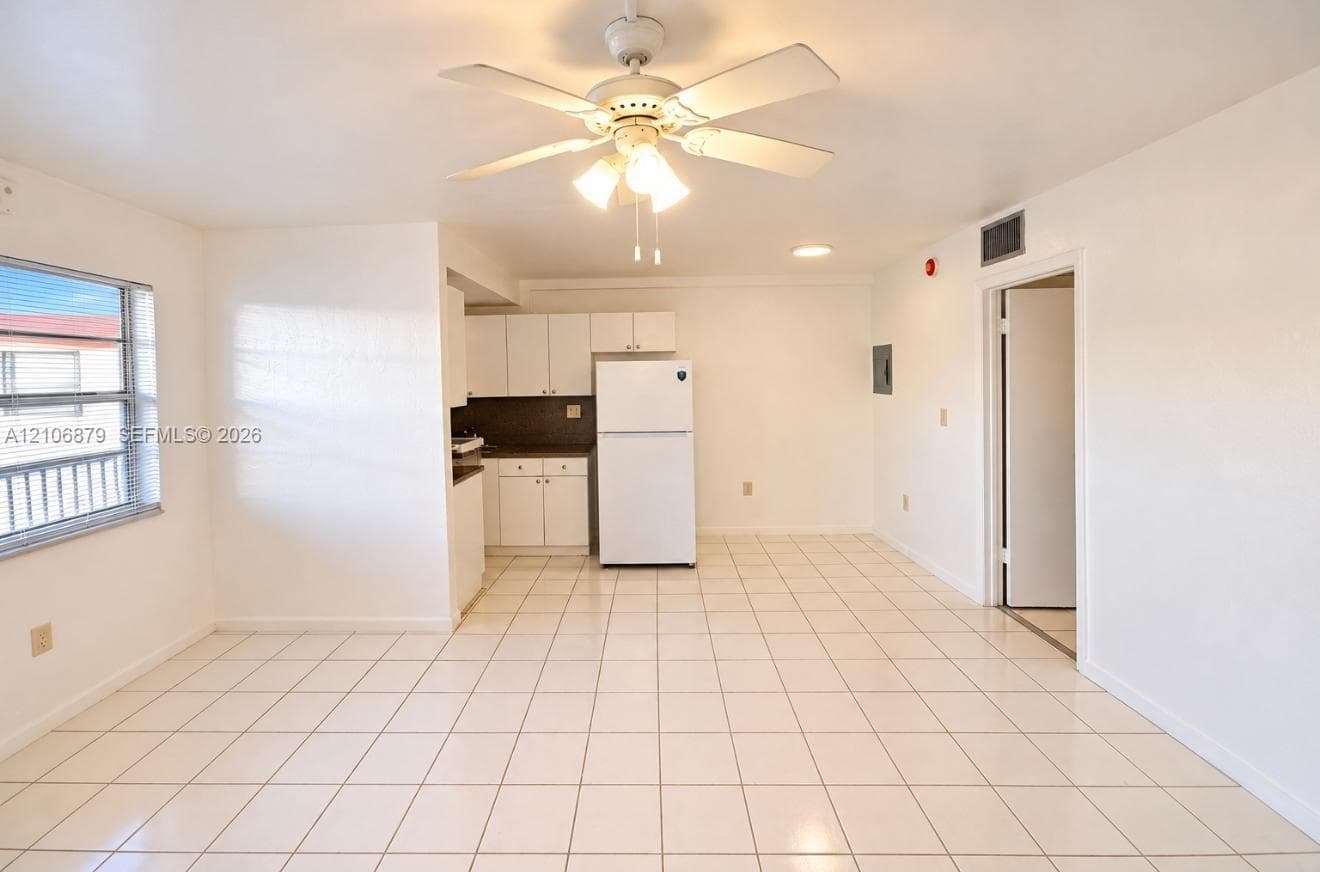Open-concept interior featuring neutral ceramic tile flooring, white cabinetry, a multi-light ceiling fan, and large windows providing natural illumination