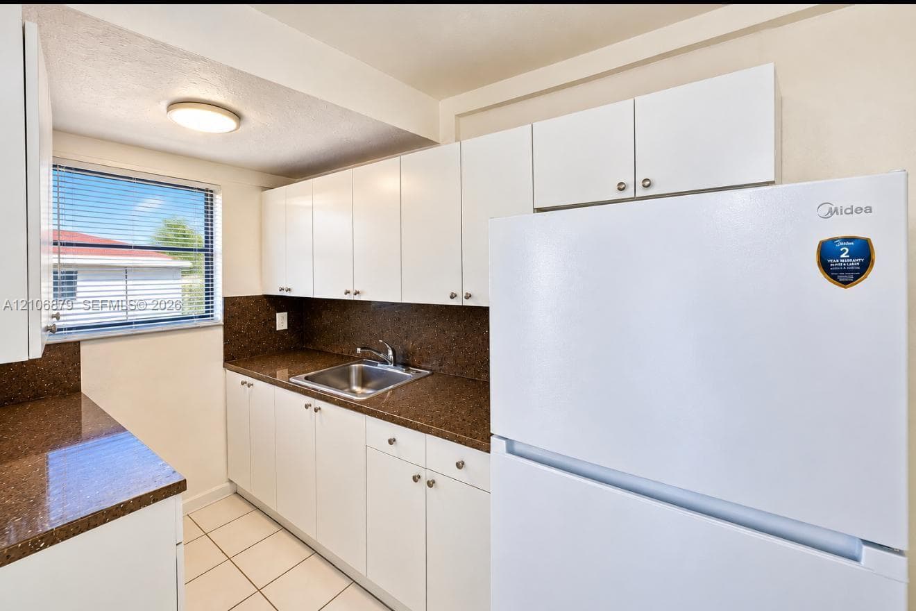Kitchen featuring white cabinetry, dark stone-finish countertops, stainless steel sink with metal faucet, and tile flooring