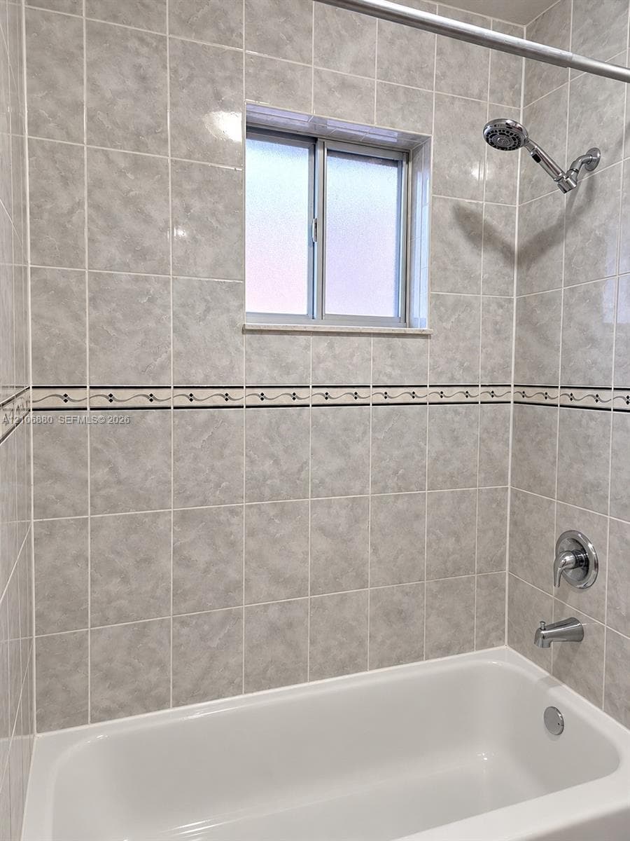 Shower and tub combination featuring full-height neutral ceramic tile surround, decorative accent tile border, chrome showerhead, and sliding window.