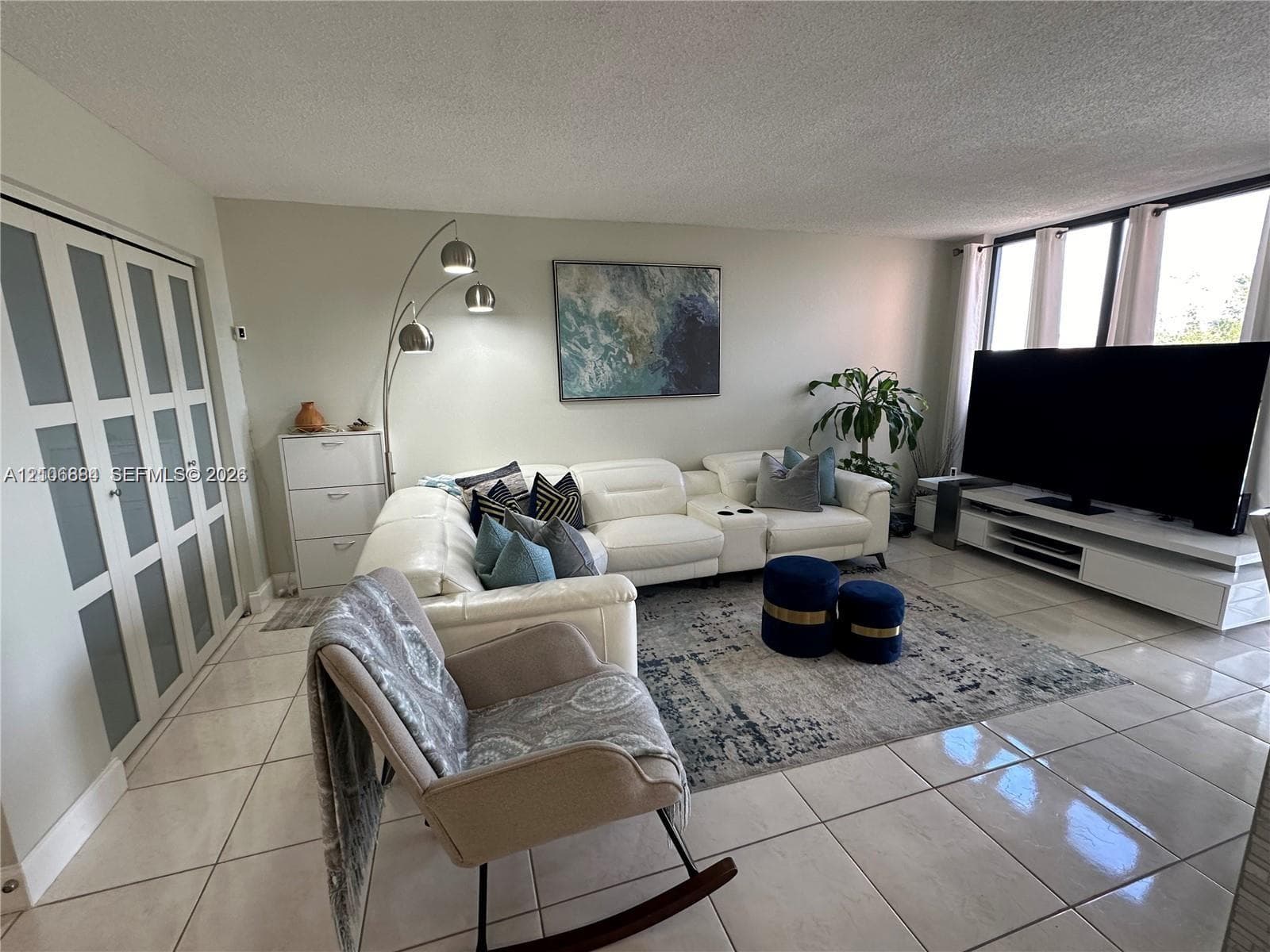 Open-concept room featuring light-toned tile flooring, floor-to-ceiling windows with window treatments, and closet doors with glass panel inserts