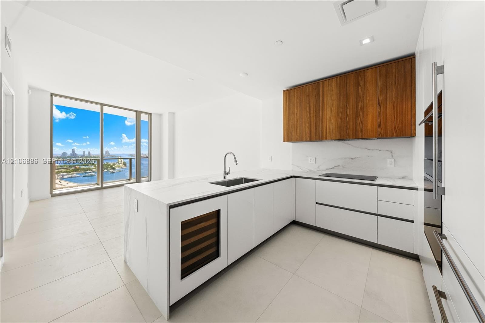 Modern kitchen featuring matte white cabinetry, wood-finish upper cabinetry, stone-surface countertops with matching backsplash, built-in wine refrigeration, and floor-to-ceiling windows