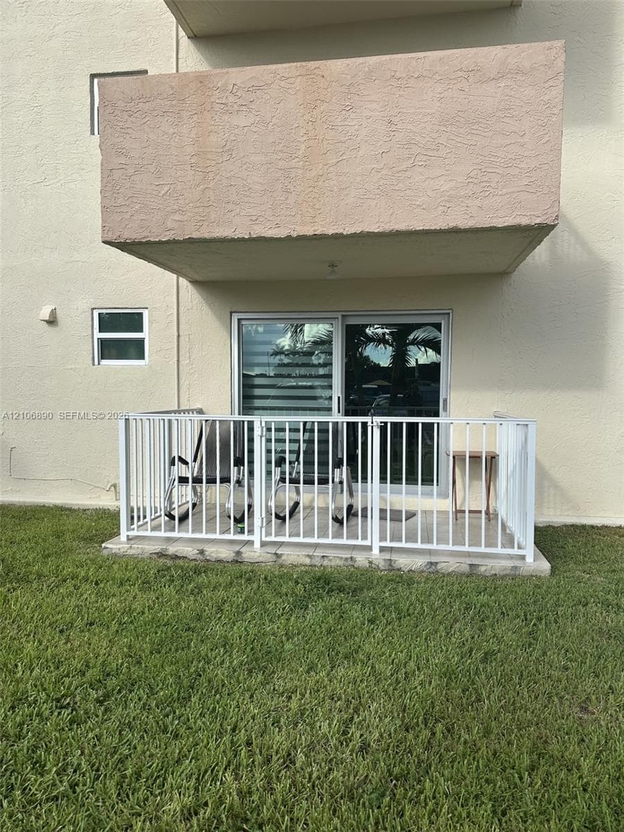 Ground-level patio enclosed by white metal railings, featuring sliding glass door access and concrete slab flooring