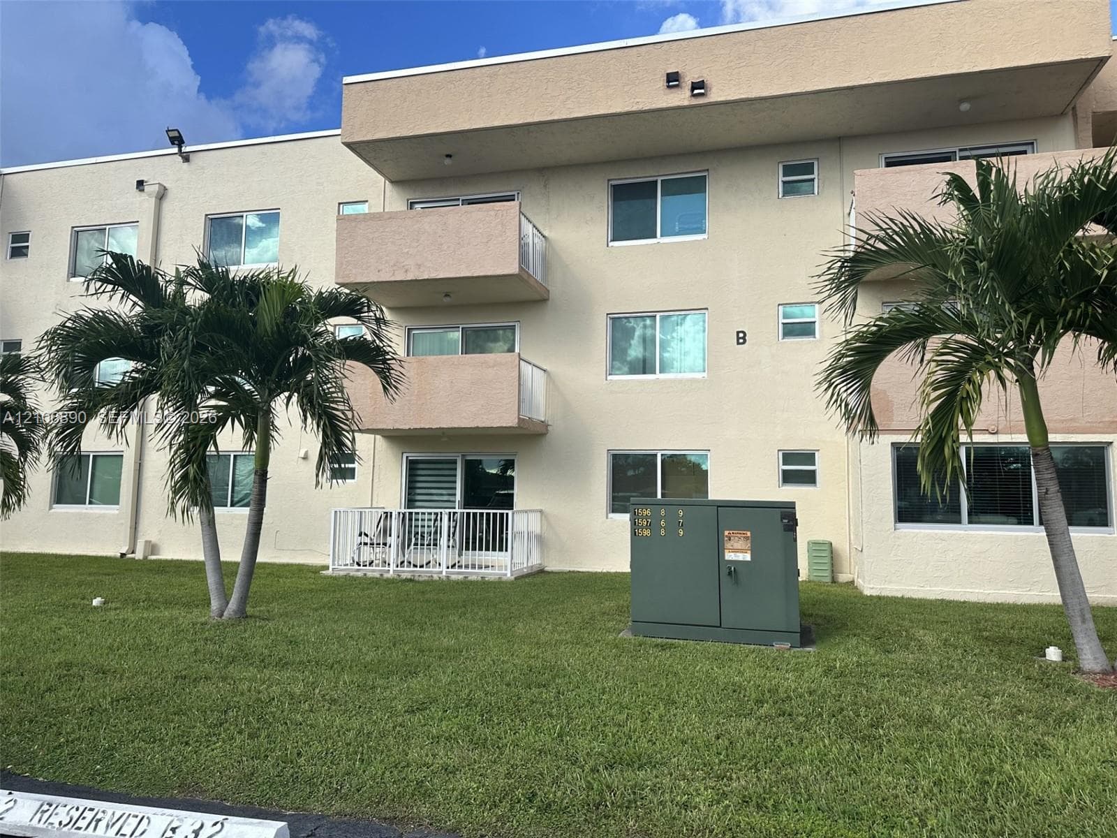 Stucco exterior building featuring multiple balconies with metal railings, sliding glass doors, and established palm trees