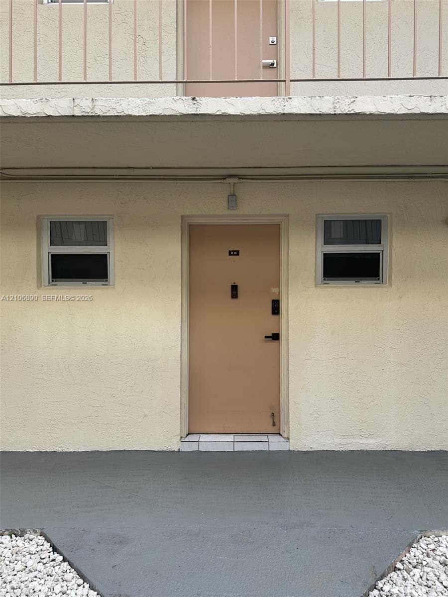Stucco exterior featuring dual slider windows, a solid-core entry door with electronic hardware, and a paved concrete landing