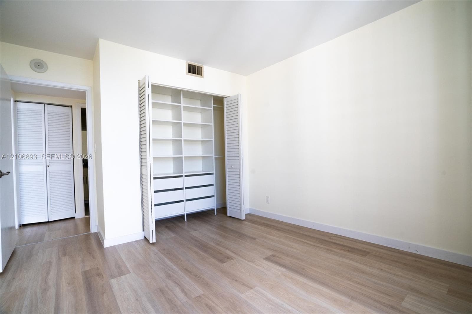 Room featuring wood-finish flooring, built-in shelving with integrated drawers, and dual louvered closet doors
