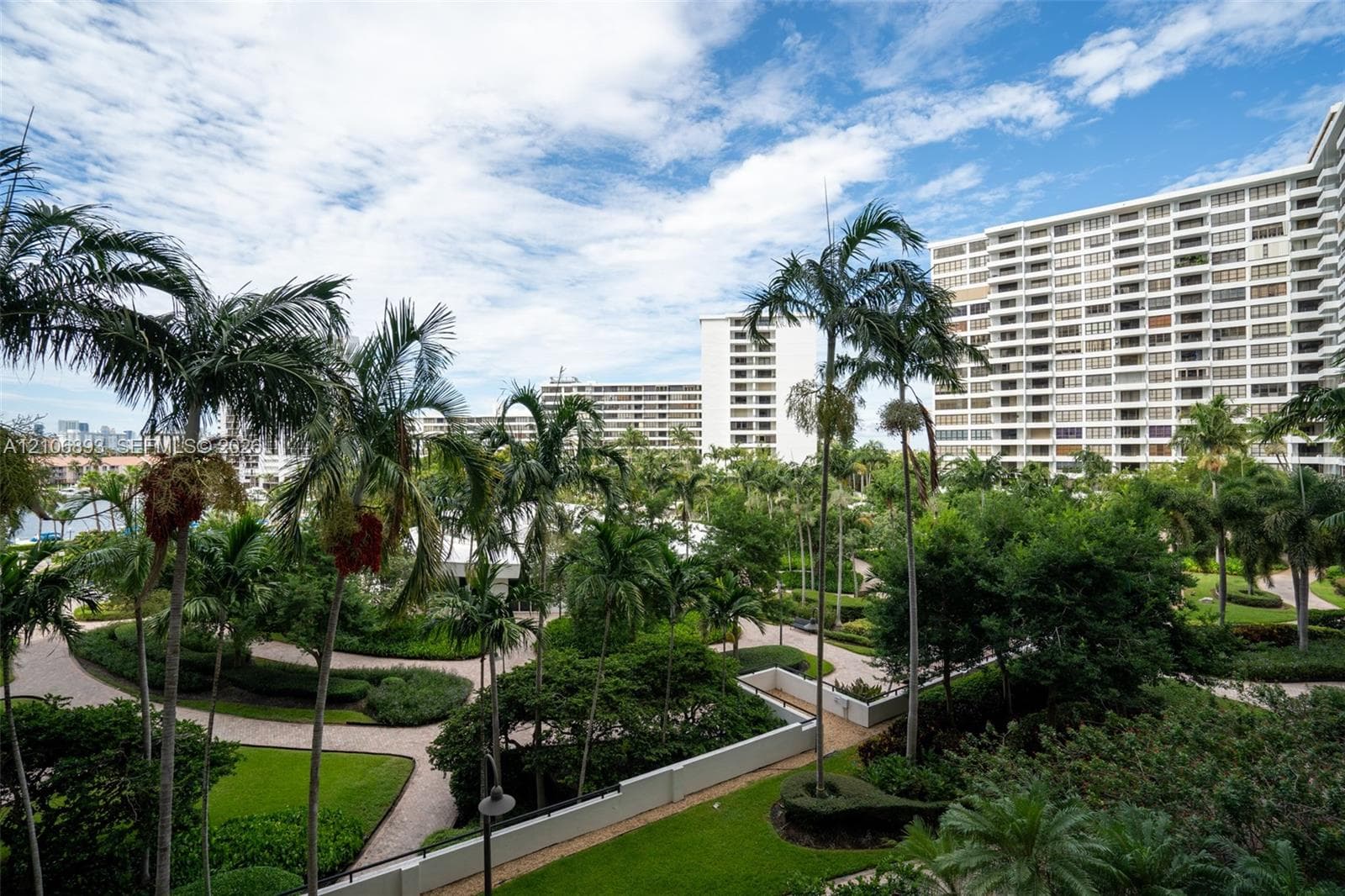 Landscaped courtyard featuring manicured lawns, mature palm trees, winding paved pathways, and perimeter low-profile concrete walls