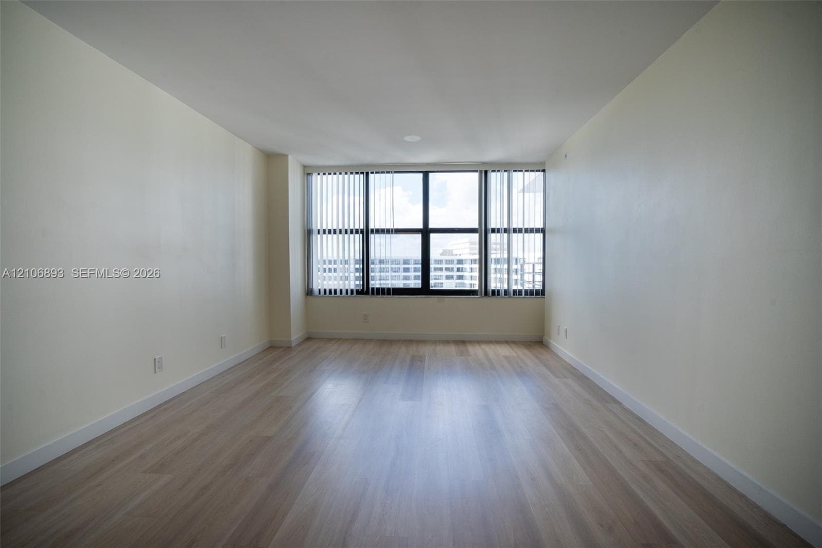 Interior room featuring wood-finish flooring, neutral wall tones, and expansive floor-to-ceiling windows with vertical blinds