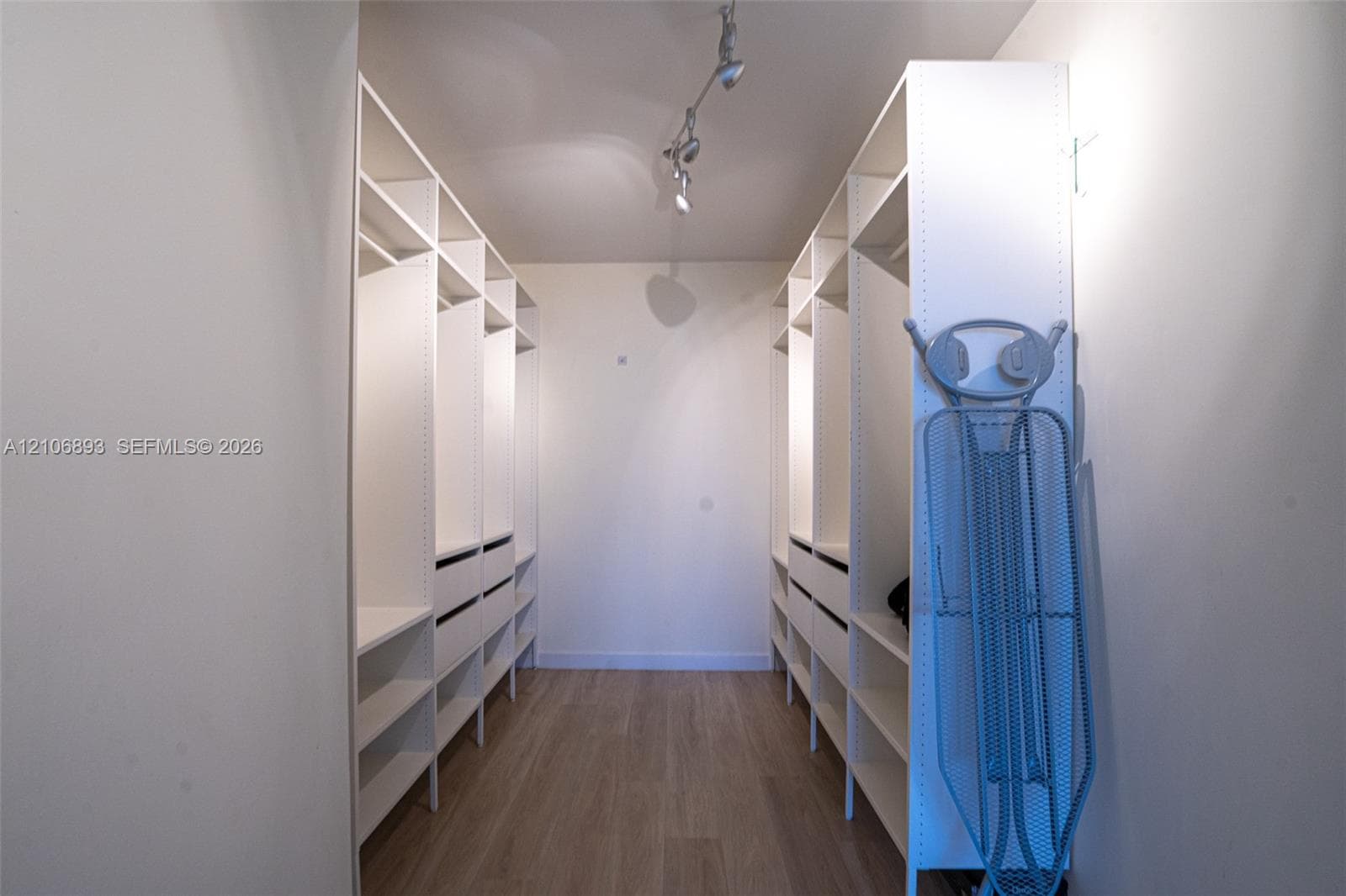 Custom walk-in closet featuring extensive built-in cabinetry, multiple hanging sections, integrated shelving, pull-out drawers, and track lighting over wood-finish flooring