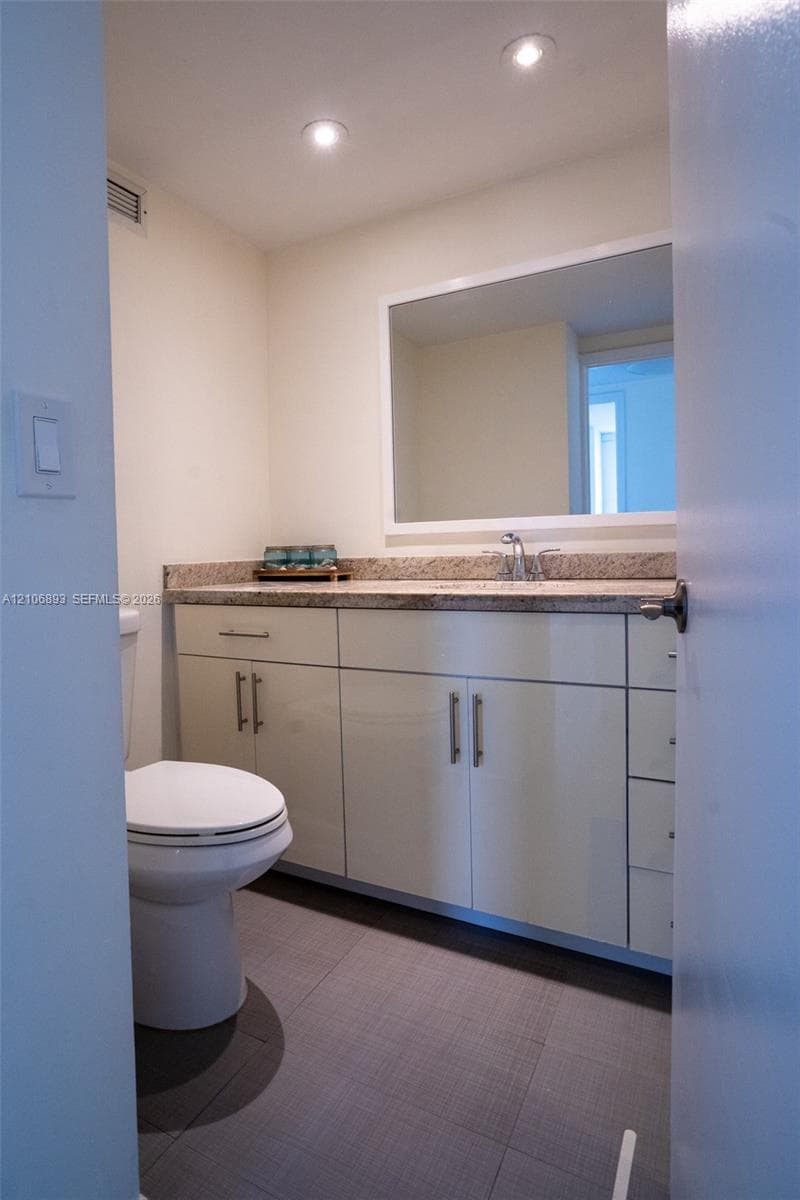Bathroom featuring a white cabinetry vanity, stone-finish countertop with an integrated basin, large rectangular wall-mounted mirror, and tile flooring