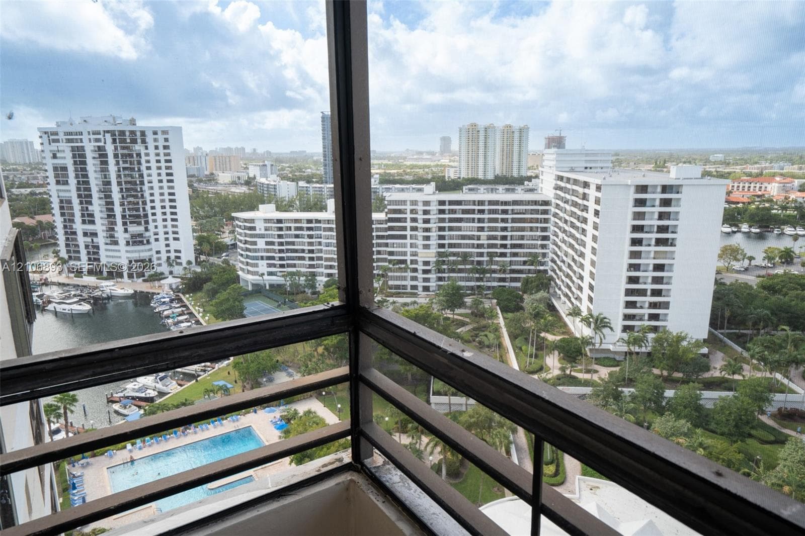 Enclosed balcony featuring metal railing and panoramic exterior perspective of the marina, swimming pool, and surrounding urban landscape