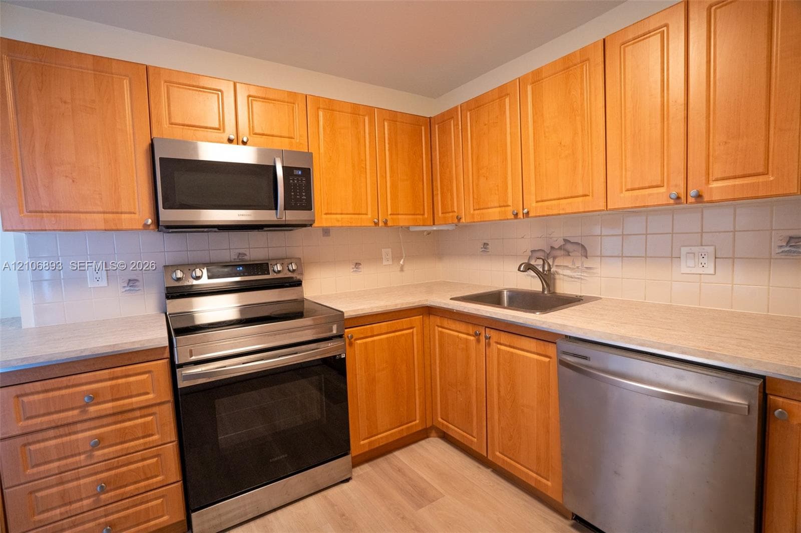 Kitchen featuring natural wood-finish cabinetry, stainless steel appliances, neutral laminate countertops, a ceramic tile backsplash, and light-toned wood-finish flooring