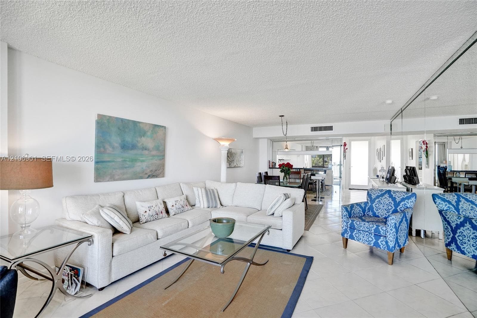 Open-concept living space featuring large-format ceramic tile flooring, full-wall mirrored accent, and textured ceiling finish