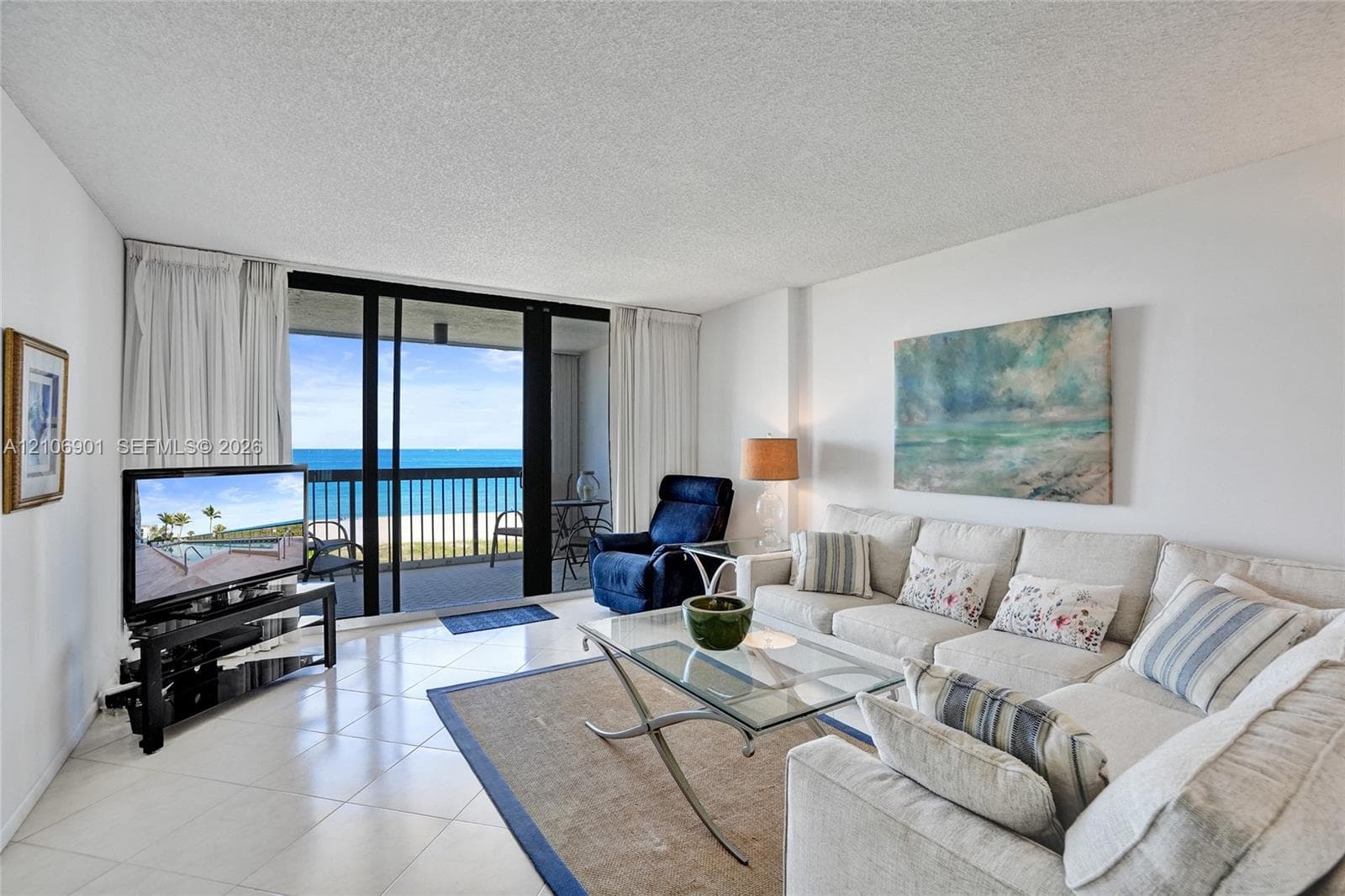 Living area featuring ceramic tile flooring, floor-to-ceiling glass sliding doors, and a covered balcony with a metal railing