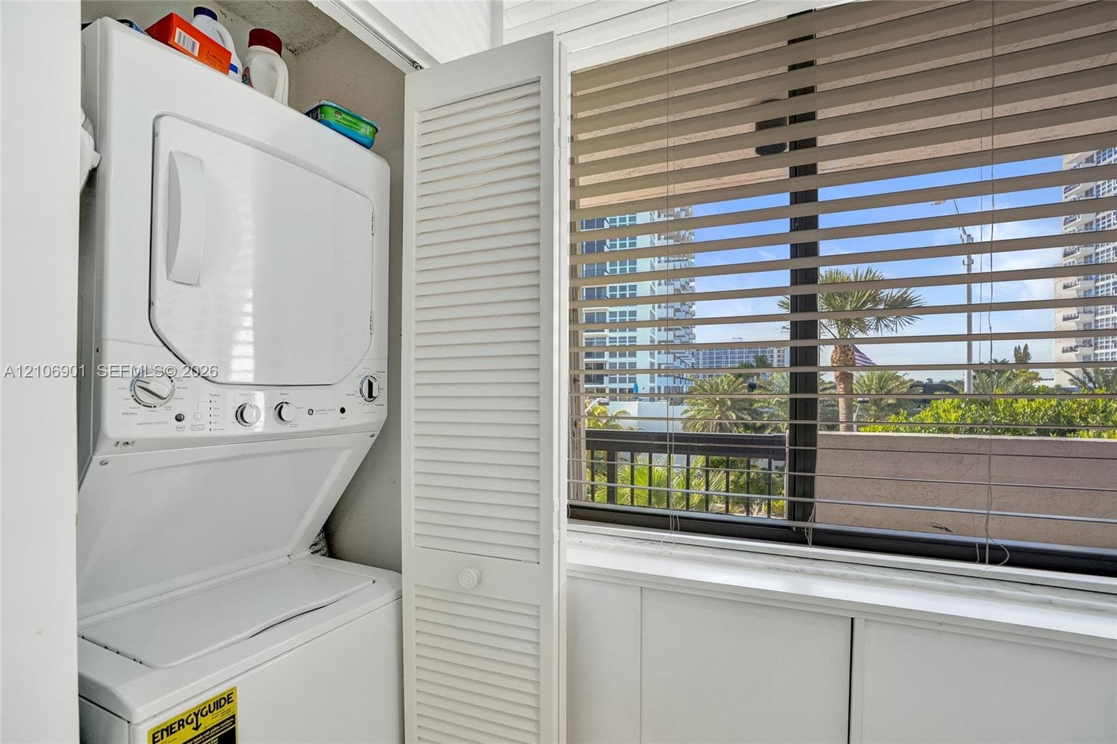 Stacked laundry unit featuring louvered bi-fold doors and large window with horizontal blinds