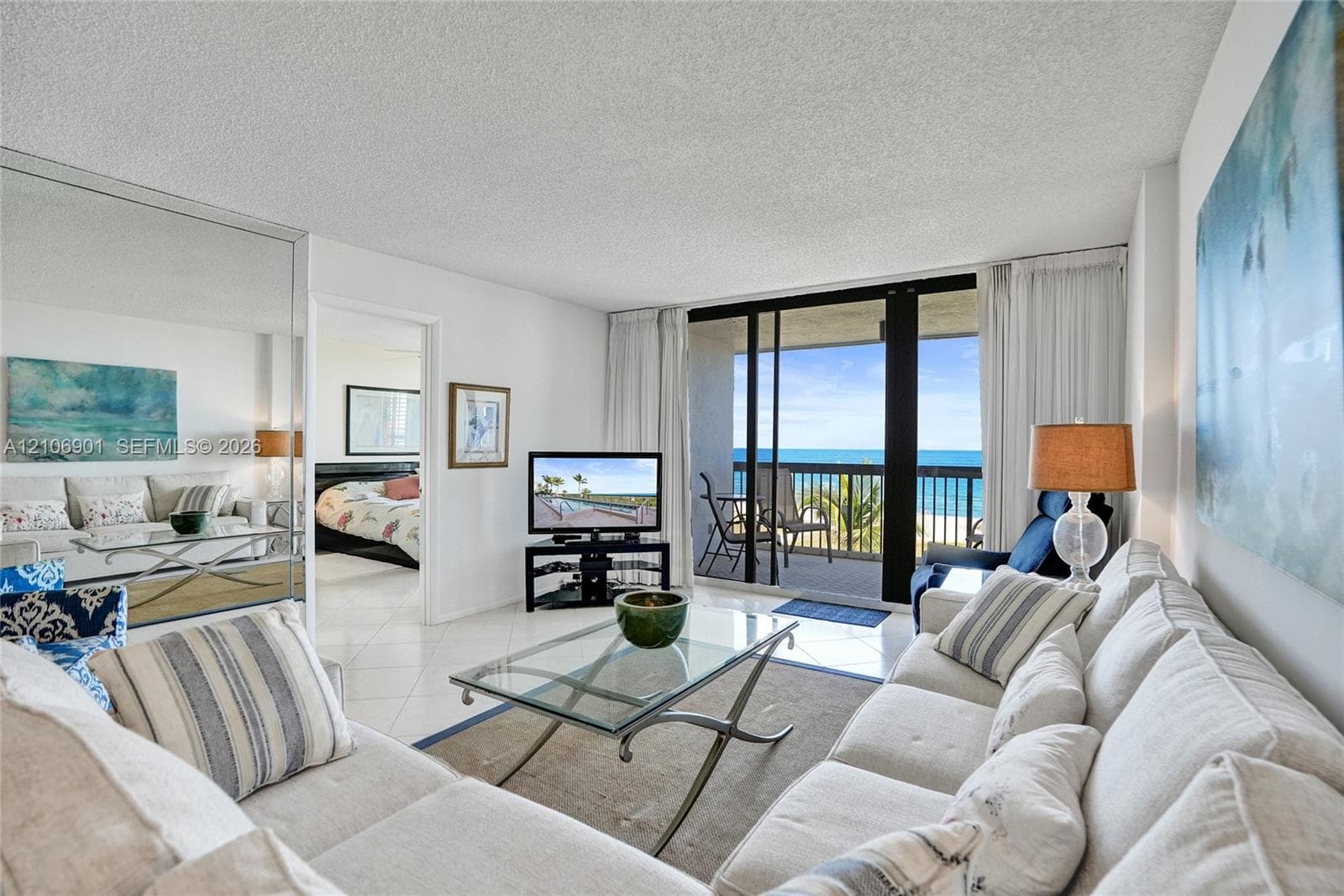 Living area featuring tile flooring, floor-to-ceiling mirrored walls, and sliding glass doors opening to an outdoor balcony with ocean scenery