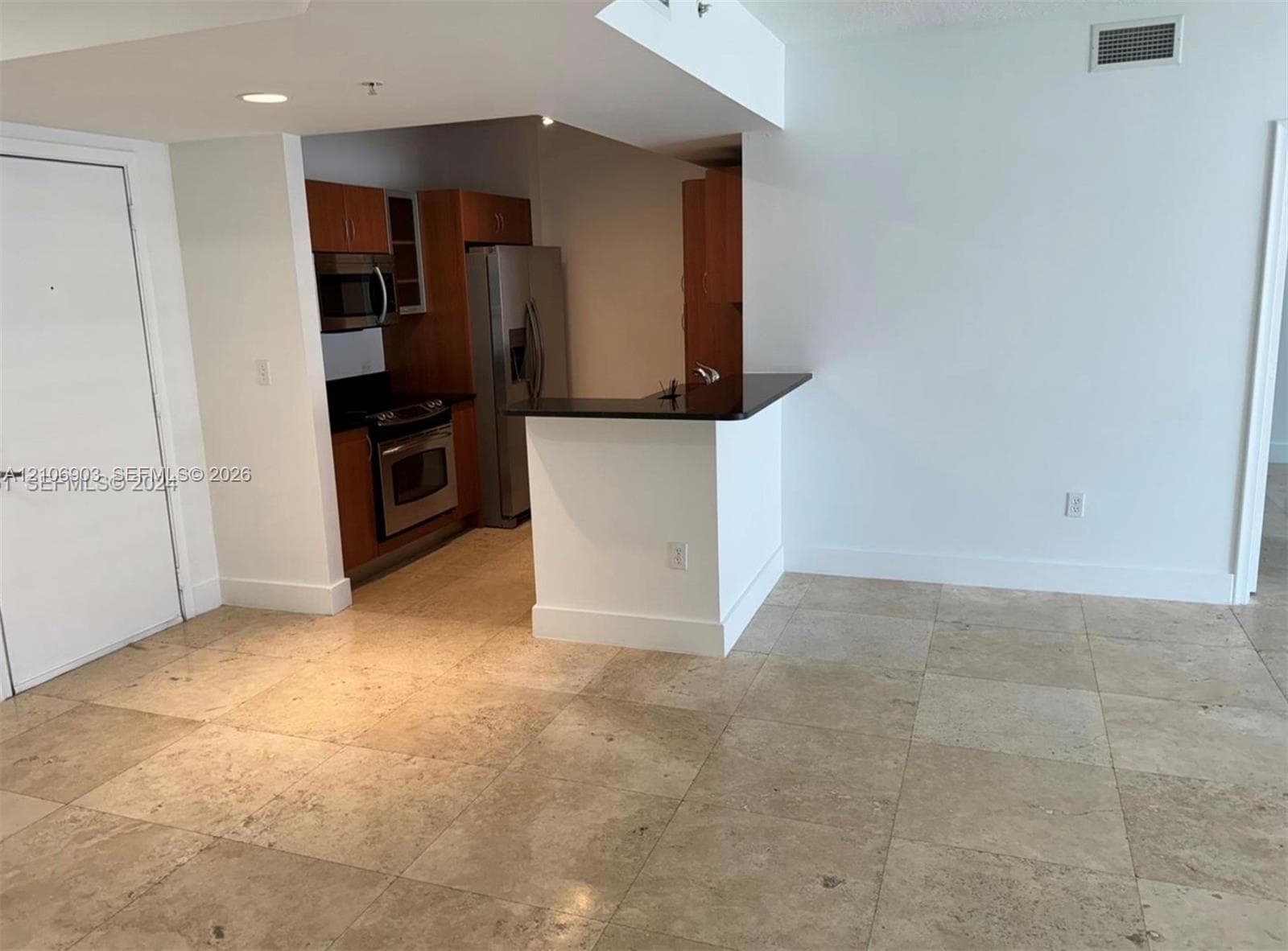 Kitchen featuring wood-finish cabinetry, stainless steel appliances, and a dark-toned countertop island with a breakfast bar