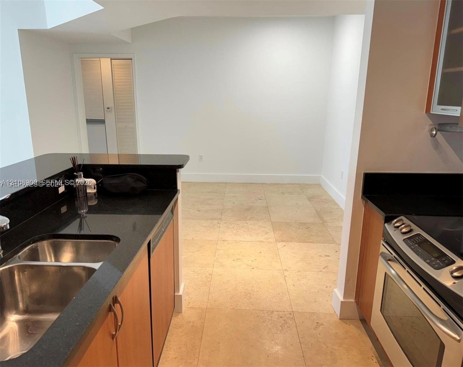 Kitchen featuring dark stone countertops, natural wood-finish cabinetry, stainless steel oven, dual-basin stainless steel sink, and oversized light-toned tile flooring