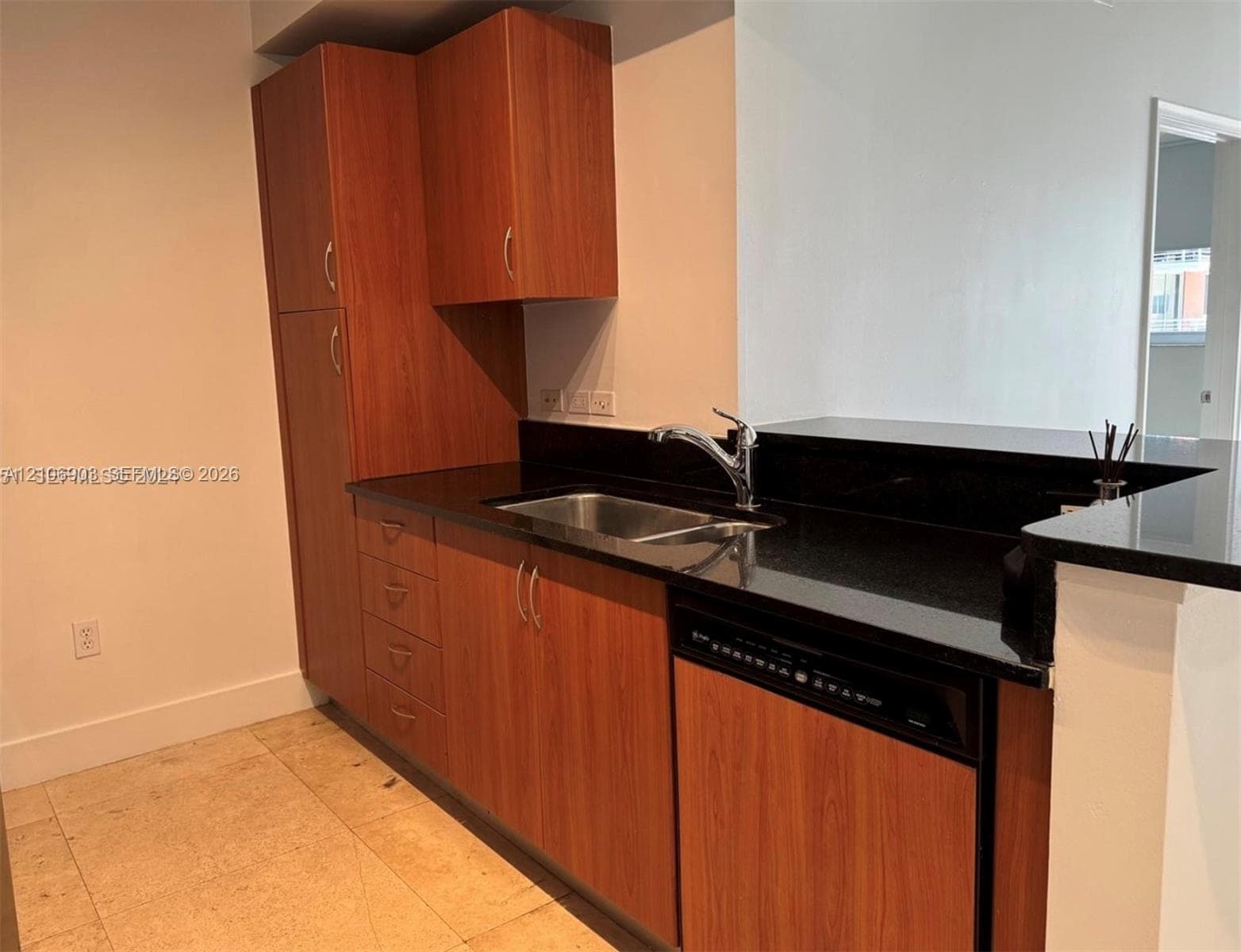 Kitchen featuring wood-finish cabinetry, black stone-surface countertops, integrated stainless steel sink with a high-arch faucet, and a built-in dishwasher