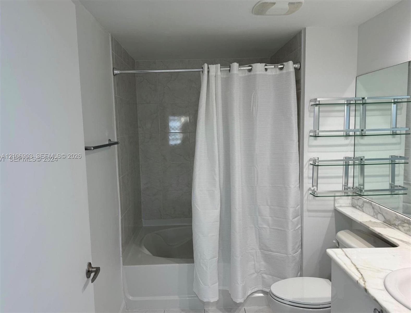 Bathroom featuring a tub-shower combination with tile surround, stone-top vanity, wall-mounted glass shelving, and a large-format mirror