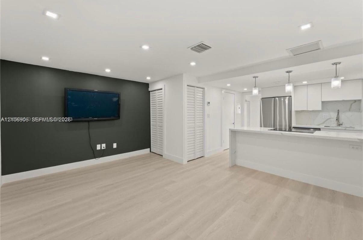 Open-concept interior featuring wood-finish flooring, recessed lighting, white cabinetry, stainless steel appliances, and a quartz-topped peninsula