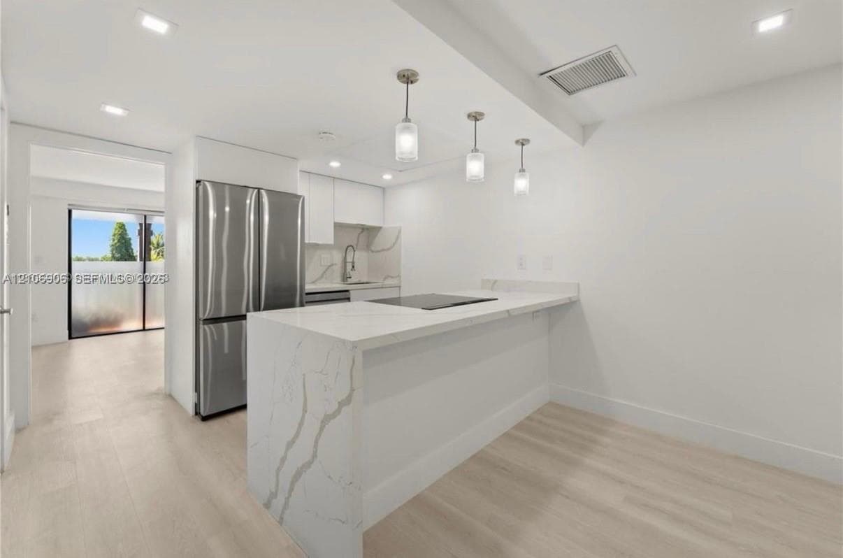 Kitchen featuring a stone-surface waterfall island, stainless steel refrigerator, recessed lighting, pendant fixtures, and wood-finish flooring