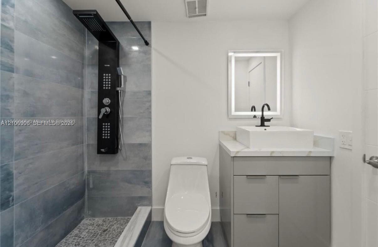 Bathroom featuring a matte black shower panel, rectangular vessel sink on a stone-topped vanity, LED-backlit mirror, and blue-toned tile shower surround