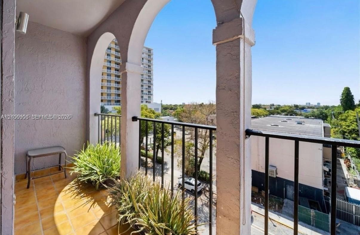 Covered balcony featuring arched stucco columns, tile flooring, and black metal railings