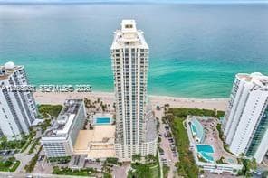 High-rise coastal residential tower featuring multi-story glass balconies, ground-level outdoor swimming pools, and direct oceanfront access