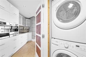 High-gloss white cabinetry, integrated stainless steel appliances, stacked laundry unit, and a paneled wood-finish door